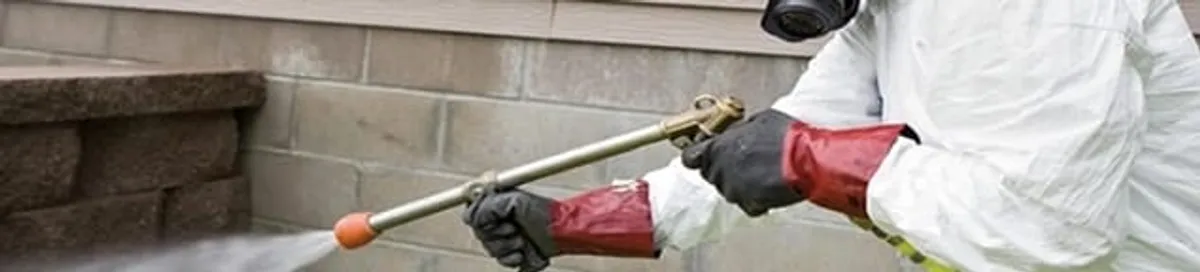 Pest control technician applying exterior insect treatment along a home foundation in Columbus, GA