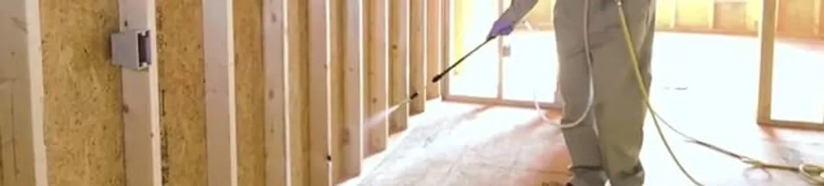 Termite treatment technician applying spray along framing and unfinished walls in Columbus, GA